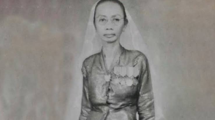 Black-and-white portrait of a woman wearing a veil and a medal-decorated dress, facing the camera.