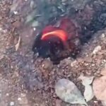 Red-hot ember glowing in a dirt hole, surrounded by small rocks and dry leaves.