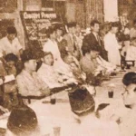 Crowded formal meeting with many people seated around a long table in a sepia-toned vintage photograph.