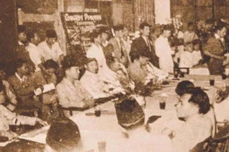Crowded formal meeting with many people seated around a long table in a sepia-toned vintage photograph.