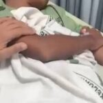 Parent gently holding a newborn wrapped in a white blanket in a hospital bed.