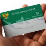 Hand holding a green Kartu Indonesia Sehat health card with the Indonesian map graphic on it.