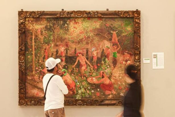 Two visitors observe a large ornate-framed painting in a museum, showing a lush garden scene with people by a water feature in the background.