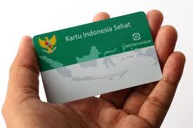 Hand holding a green Kartu Indonesia Sehat health card with the Indonesian map graphic on it.
