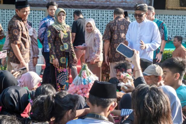 Group of people in batik attire posing at an outdoor ceremony, with audience members taking photos nearby.
