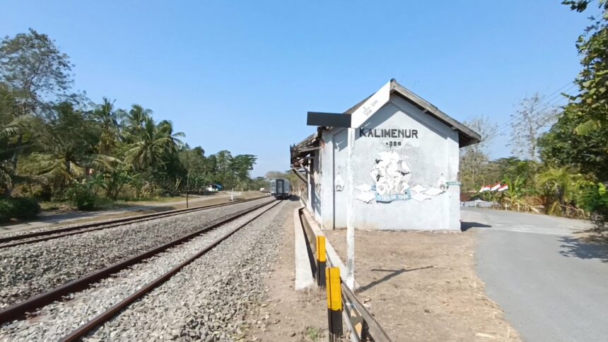 img-5335353 - Mabur.co Rural railway platform with a small white station shed beside the tracks and trees under a clear blue sky.