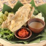 Fried fish on banana leaves with lime slices, served with chili sauce and dipping sauce.