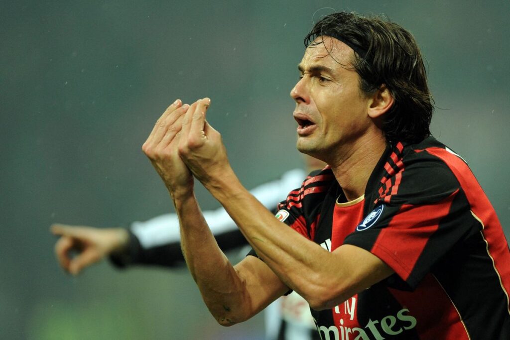 Soccer player in red-and-black kit making a praying/peacemaking gesture during a match