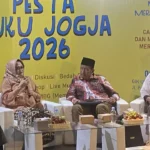 Panel discussion on a bright yellow backdrop that reads 'Pesta Buku Jogja 2026,' with four people seated in white chairs and a woman in a hijab speaking into a microphone.