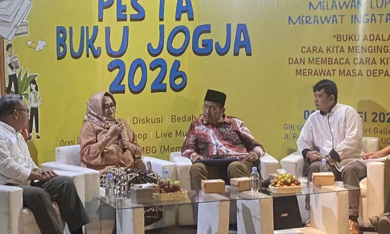 Panel discussion on a bright yellow backdrop that reads 'Pesta Buku Jogja 2026,' with four people seated in white chairs and a woman in a hijab speaking into a microphone.
