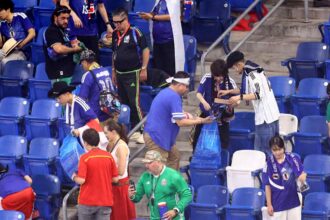 Group of fans in blue jerseys gathering in stadium seats, some holding bags and drinks.
