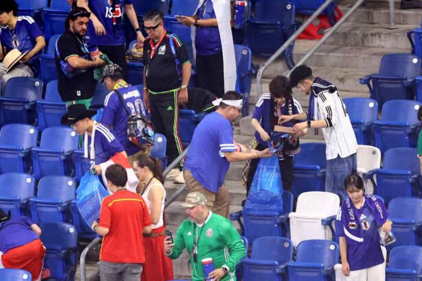 Group of fans in blue jerseys gathering in stadium seats, some holding bags and drinks.