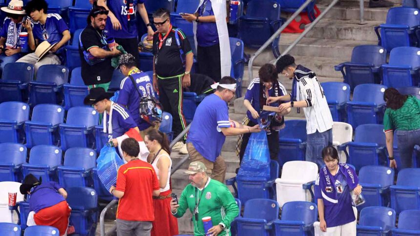 japanese cleaning up stadium after Tunisia game by nikkei asia - Mabur.co Group of fans in blue jerseys gathering in stadium seats, some holding bags and drinks.