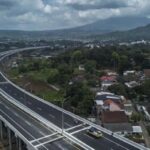 Aerial view of a curved elevated highway passing over a residential town with green hills in the distance.