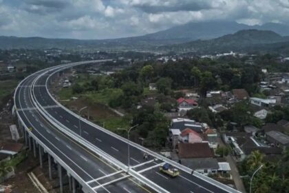 Aerial view of a curved elevated highway passing over a residential town with green hills in the distance.