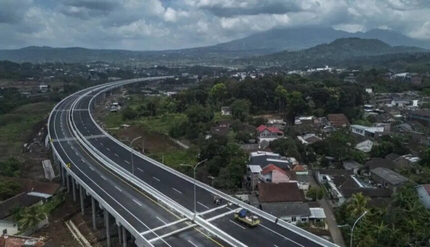 Aerial view of a curved elevated highway passing over a residential town with green hills in the distance.
