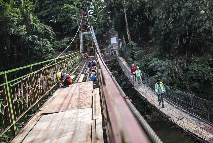 Pekerja menyelesaikan pembangunan jembatan gantung di kawasan Srengseng Sawah Jagakarsa Jakarta Jumat 38 - Mabur.co Workers wearing hard hats repair a suspension bridge in a dense forest