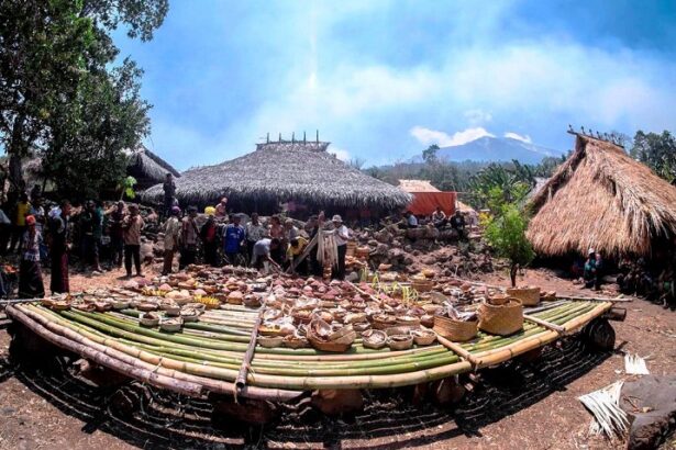 People browse a circular display of woven baskets and pottery around a bamboo platform under thatched huts in a village market setting.
