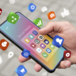 Hand holding a smartphone with a rainbow-colored screen and floating social media icons around it.