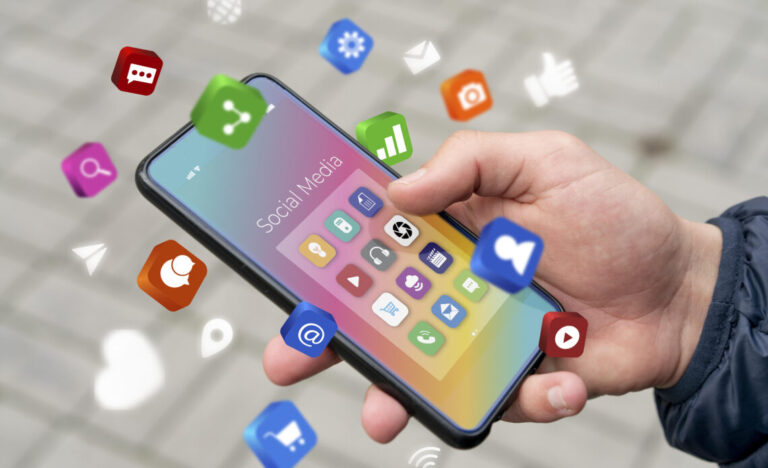 Person holds a smartphone with colorful social media app icons floating around the screen labeled 'Social Media'.