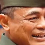 Close-up of a smiling man in a green cap, facing slightly to the right, expression warm and cheerful.