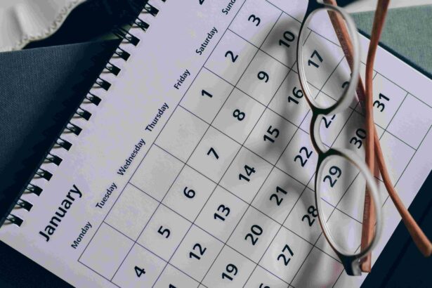 Close-up of a calendar page with a grid of dates, reading glasses resting on it and a spiral notebook in the background.