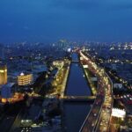 Aerial night view of a city with a central canal flanked by illuminated roads and dense, glowing buildings.
