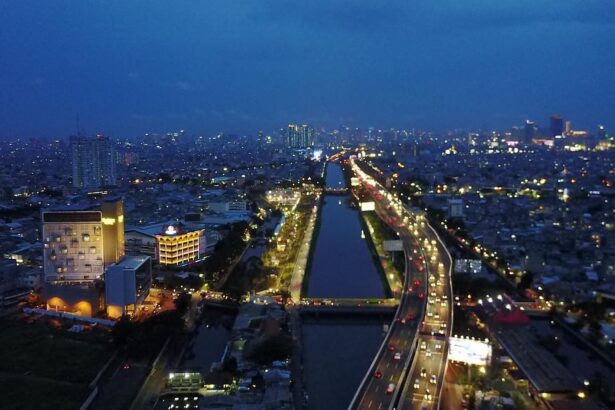 Aerial night view of a city with a central canal flanked by illuminated roads and dense, glowing buildings.