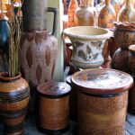 Assorted clay pots and vases with carved and painted patterns stacked and displayed in a shop window.