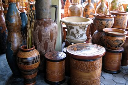 Assorted clay pots and vases with carved and painted patterns stacked and displayed in a shop window.