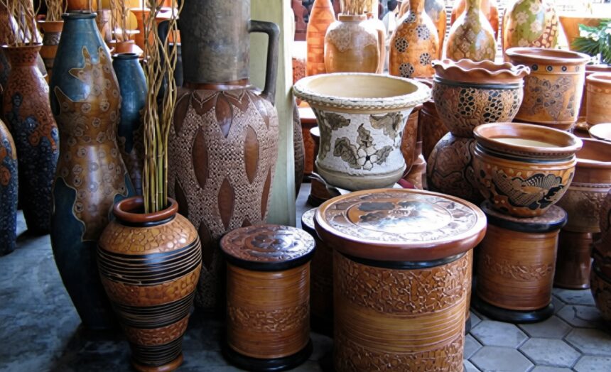 Assorted clay pots and vases with carved and painted patterns stacked and displayed in a shop window.