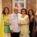 Six people in festive Indian attire pose together indoors, with a Forbes Indonesia magazine cover on the wall behind them.