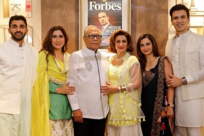 Six people in festive Indian attire pose together indoors, with a Forbes Indonesia magazine cover on the wall behind them.