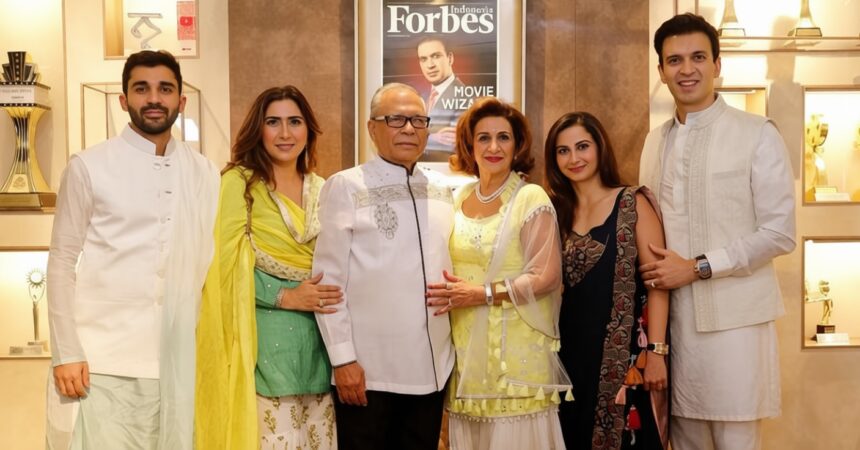 Six people in festive Indian attire pose together indoors, with a Forbes Indonesia magazine cover on the wall behind them.