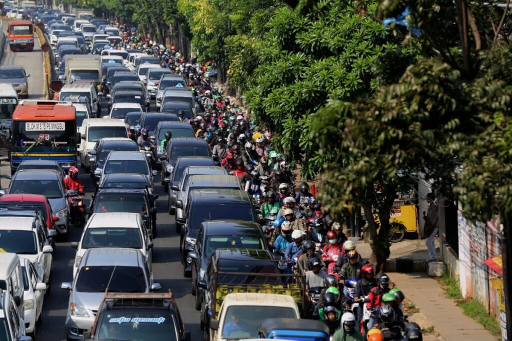 Busy city street with heavy traffic: rows of cars in the left lanes and a dense line of motorcycles along the right, beside trees.
