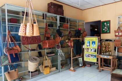 Boutique display of leather handbags and purses on metal shelves in a sunny shop interior