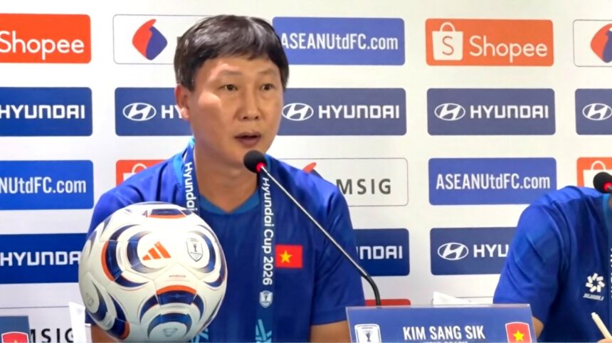 Asian man in a blue shirt speaks at a press conference with a soccer ball on the table and sponsor logos in the background, including Hyundai and Shopee.
