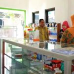 Bright shop interior with a glass display counter; three people stand near shelves of products.