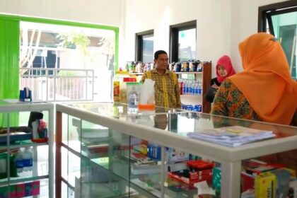 Bright shop interior with a glass display counter; three people stand near shelves of products.