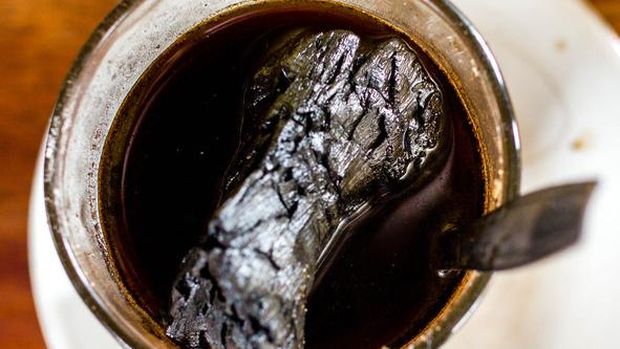 Mug of black coffee with a burnt, crumpled object floating in the liquid