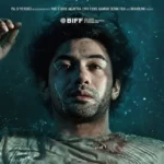 Man underwater, floating on his back with one hand above his head, moody lighting and bubbles around.