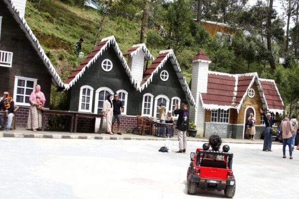 Row of chalet-style houses with white trim along a street; people chat and sit outside while a child drives a red toy car in the foreground.
