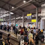 Crowded train platform at Lempuyangan station with many passengers waiting along the tracks, signs overhead.
