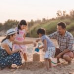 Family of four building a sandcastle on the beach at sunset, working together.