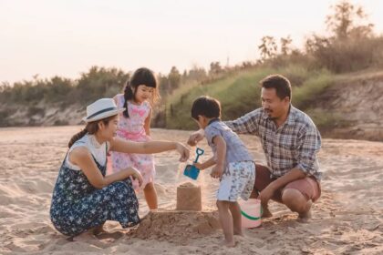 Family of four building a sandcastle on the beach at sunset, working together.