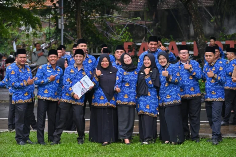 Group of colleagues in matching blue batik uniforms and black caps posing outdoors, giving thumbs up.