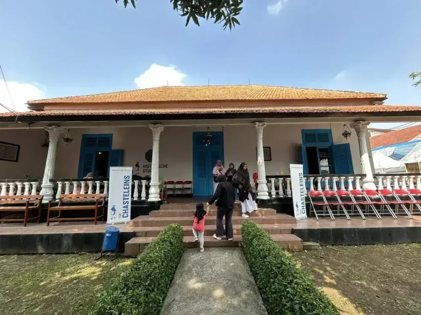 Colonial-style building with orange-tiled roof, white pillars, blue doors, and a veranda; people walk up the stone steps.