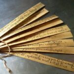 Wooden folding fan with handwritten text on each slat, tied together at the base with string.