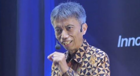 m1 - Mabur.co Speaker on stage wearing a patterned batik shirt, holding a microphone and smiling.