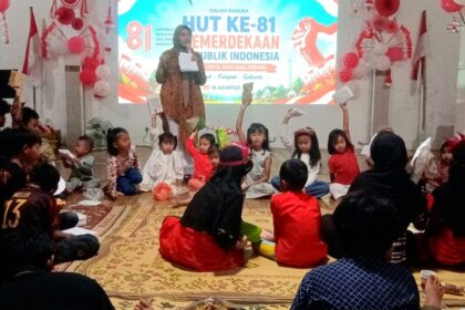 Woman on stage hosting a kids' event with a banner for HUT ke-81 Indonesia; children sit in a circle, holding papers.
